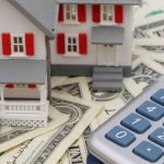 a model house sits on top of a pile of money next to a calculator