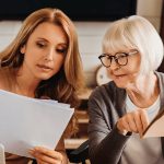 two women looking at papers with a senior lending logo in the background