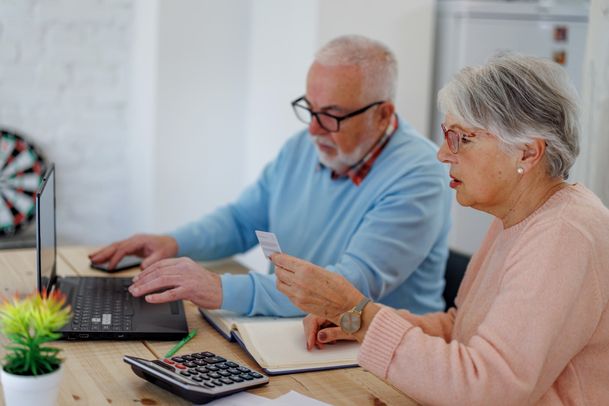an elderly couple sitting at a table with a laptop and a calculator discussing hecm