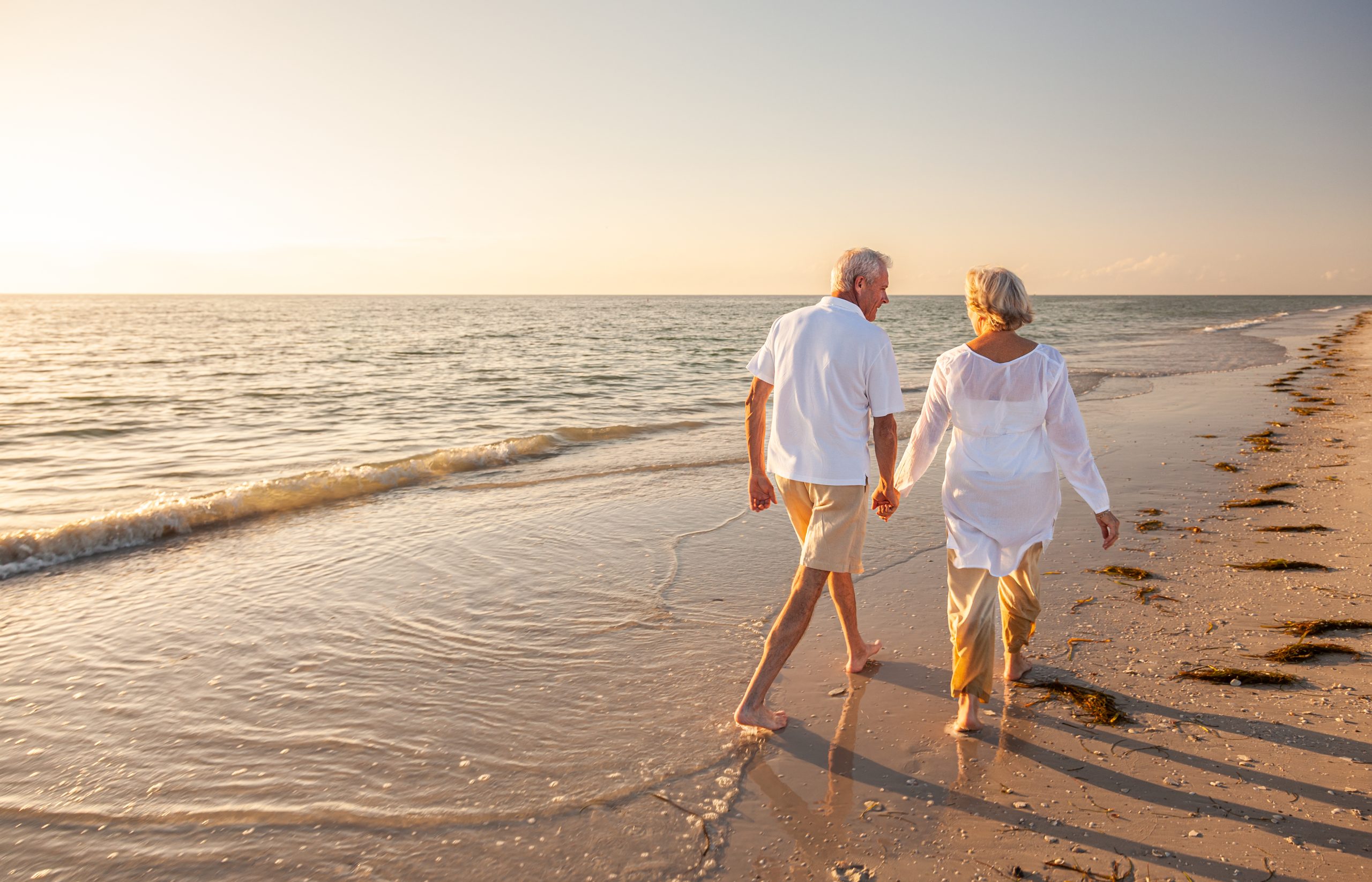 a man and woman are walking on the beach holding hands