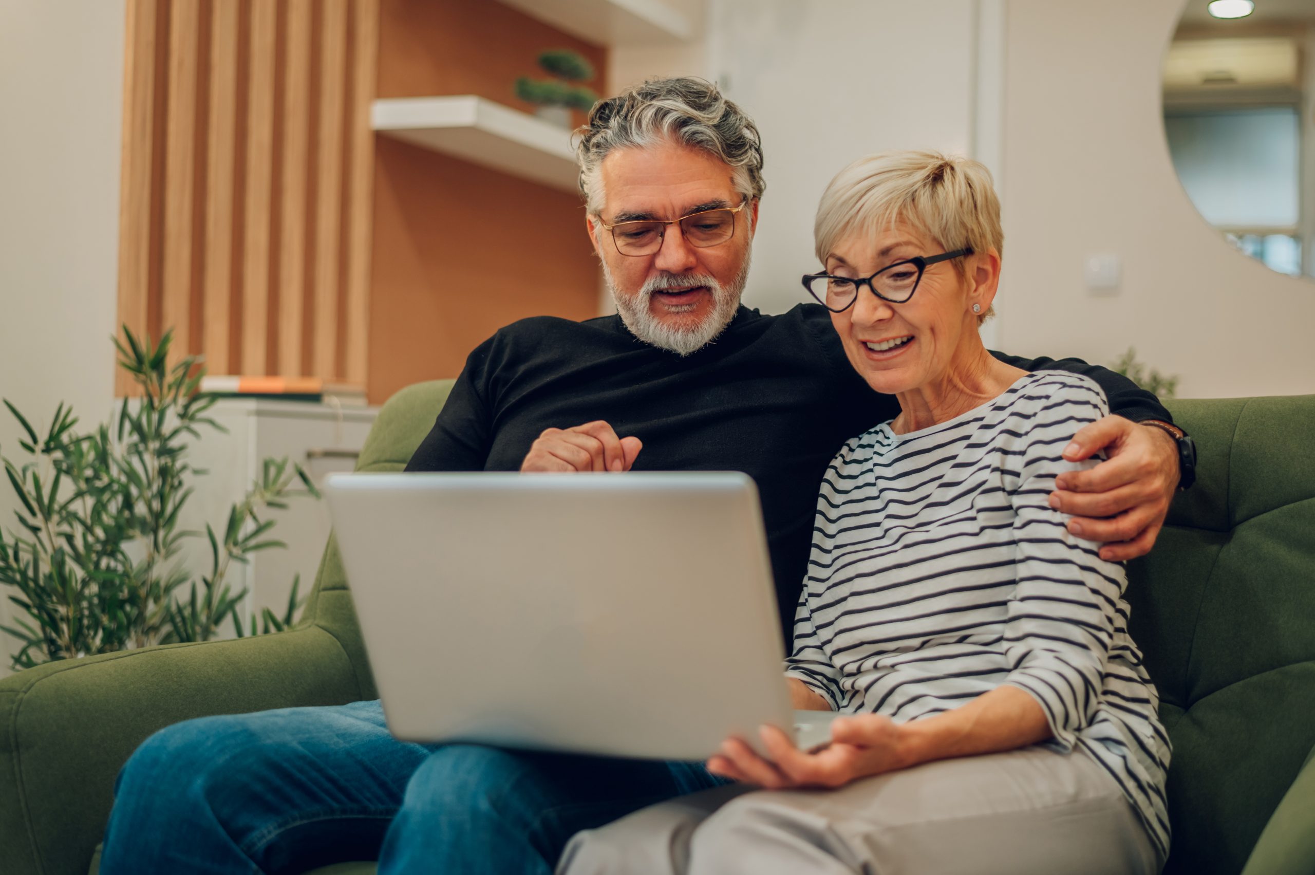 a man and woman sit on a couch looking at a laptop about reverse mortgage