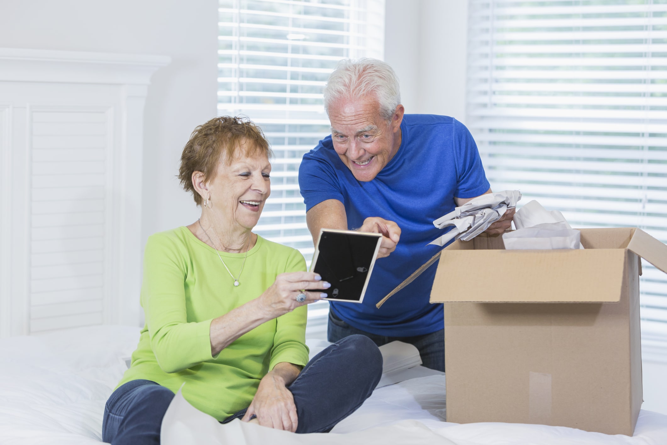 an elderly couple sitting on a bed looking at a picture