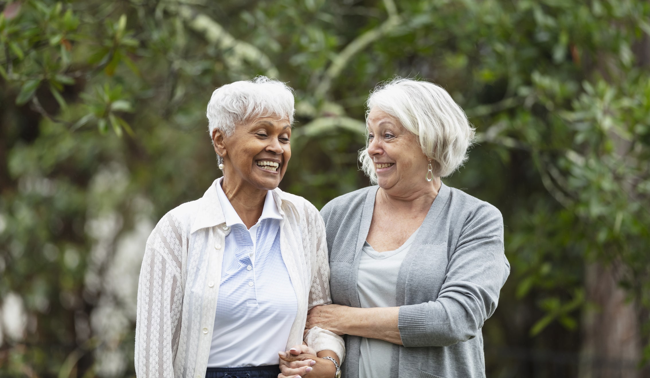 two older women standing next to each other and smiling with arms together