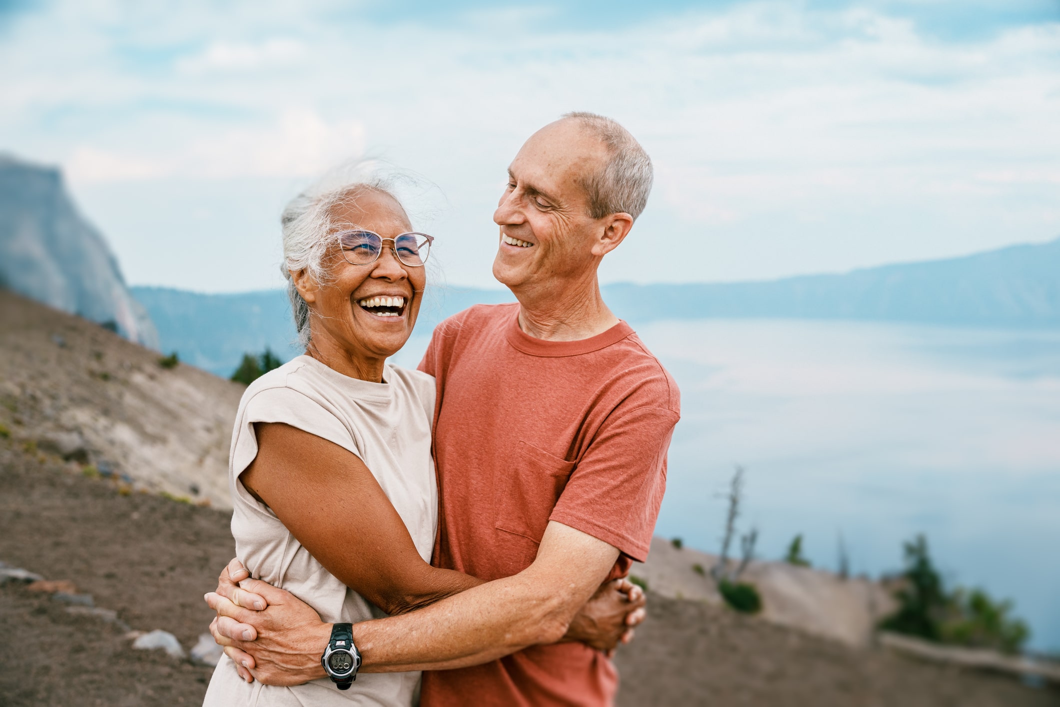 a man and woman are hugging and smiling in front of a lake