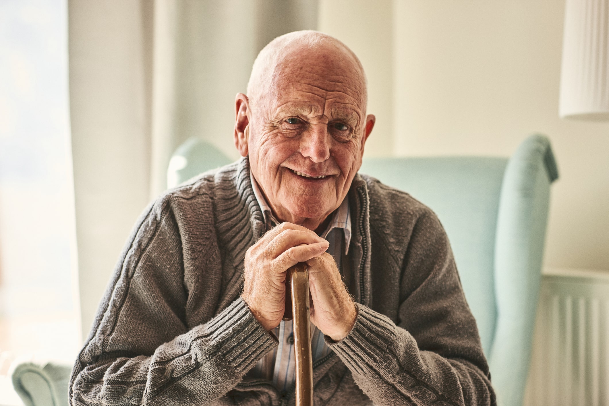 an elderly man sitting in a chair holding a cane