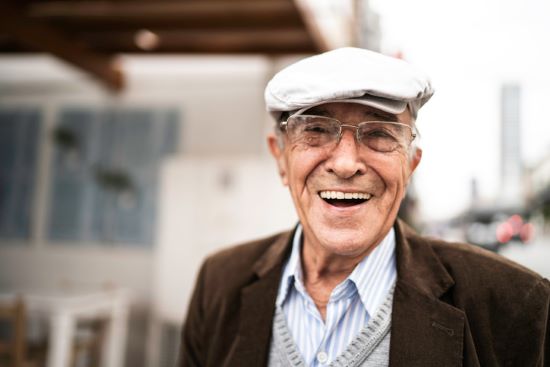 an elderly man wearing glasses and a hat is smiling for the camera .