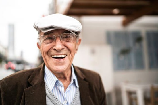 an elderly man wearing glasses and a hat is smiling for the camera