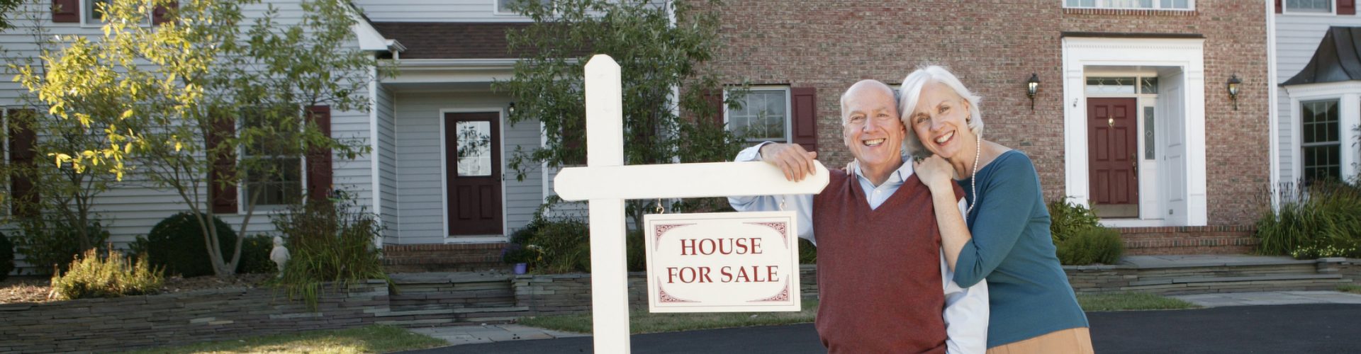 a man and woman standing in front of a house for sale sign